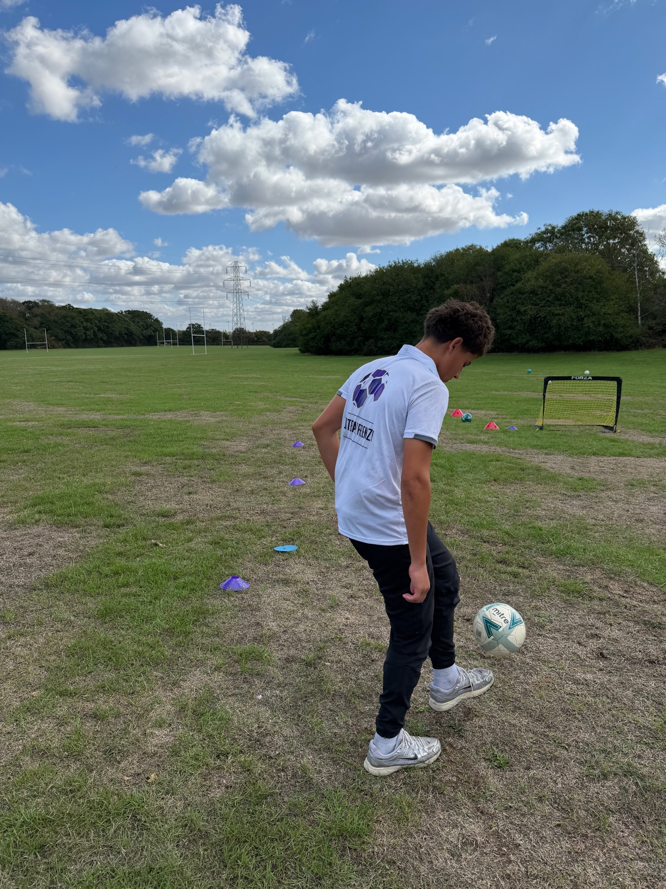 Person in a Football Frenzy shirt playing with a football on grass