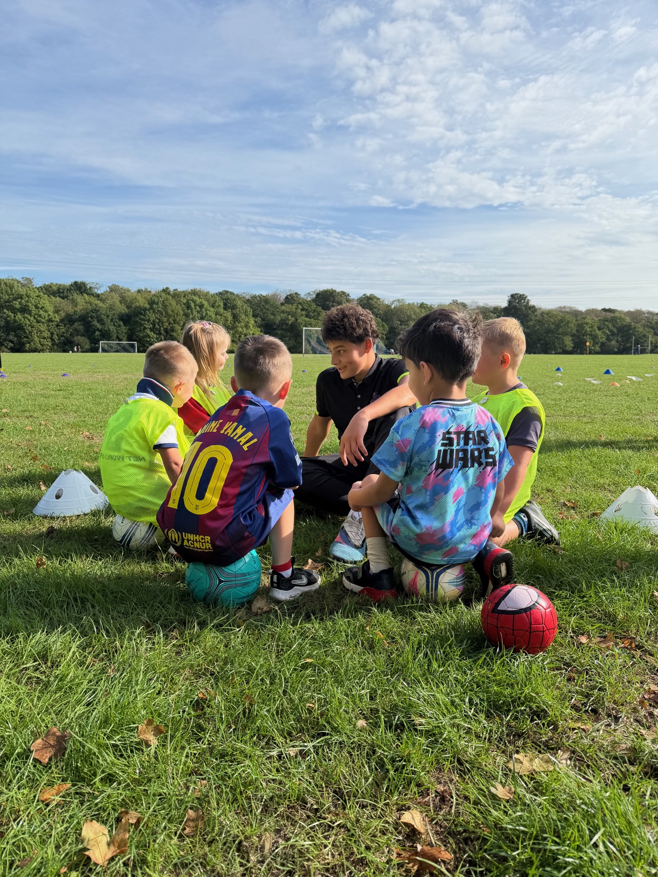 Children gathered with a Football Frenzy coach on the grass